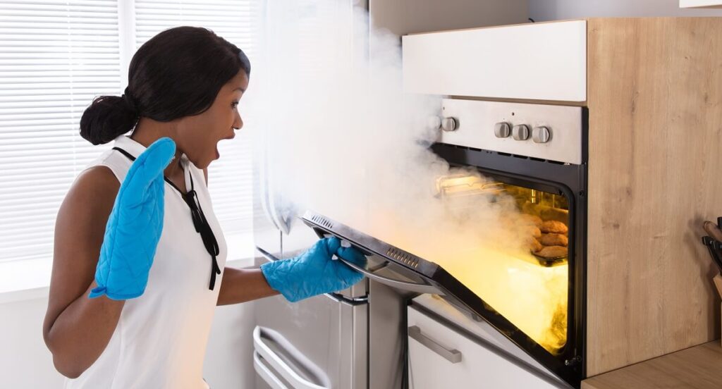woman looking at burnt cookies with smoke coming from oven