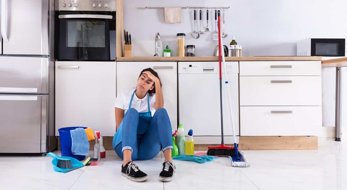 young woman sitting on kitchen floor and looking at cleaning products at home