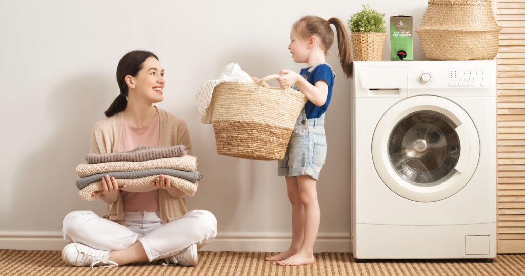 Mother and daughter at the washing machine with their laundry and the EnviroKlenz Liquid Laundry Enhancer