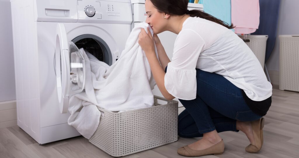 Woman smelling her fresh laundry with the EnviroKlenz Liquid Laundry Enhancer placed next to her