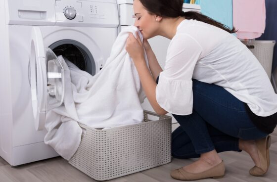 Woman smelling her fresh laundry with the EnviroKlenz Liquid Laundry Enhancer placed next to her